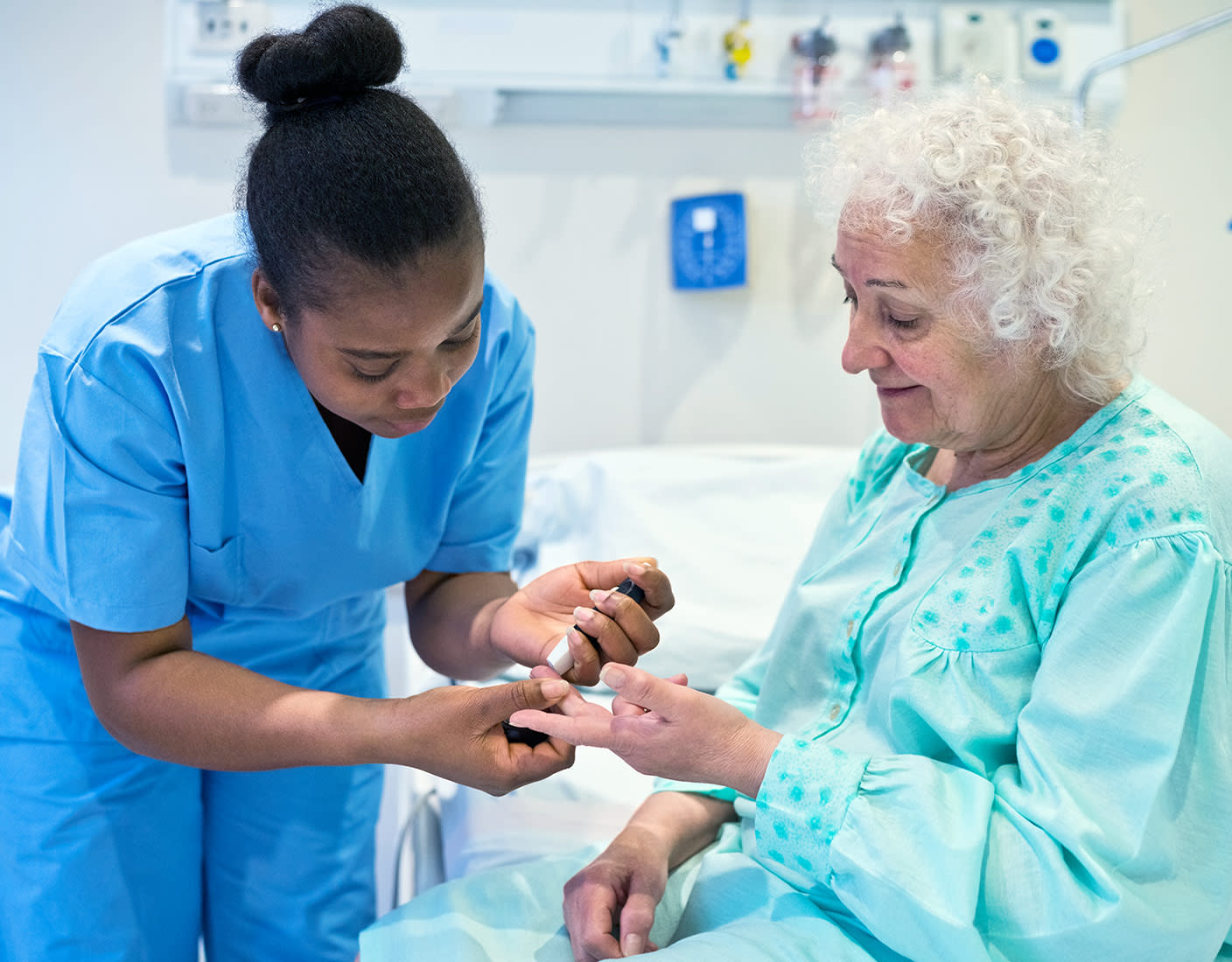 A nurse provides care to an older woman by assisting her in checking blood sugar in a healthcare setting.